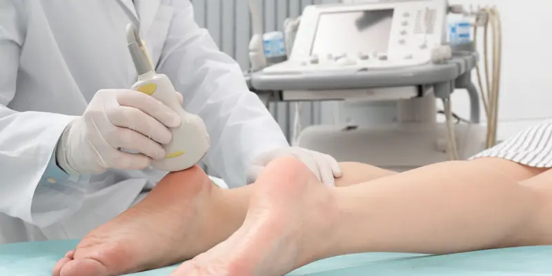 Clinician holding a probe against a patient’s heel in clinic, with the treatment machine alongside